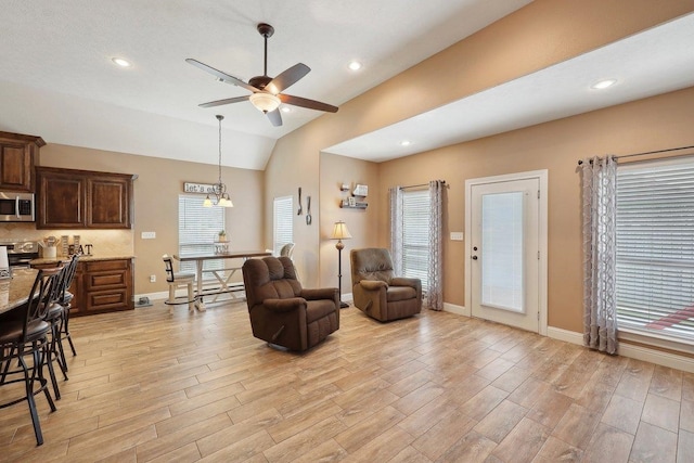 living room with a ceiling fan, light wood finished floors, healthy amount of natural light, baseboards, and vaulted ceiling