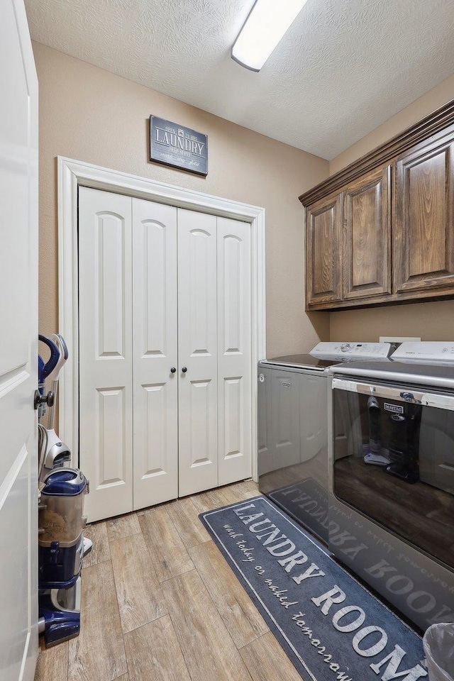 laundry area featuring washer and dryer, light wood-style flooring, cabinet space, and a textured ceiling