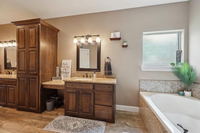 full bathroom featuring a garden tub, two vanities, baseboards, and wood finished floors