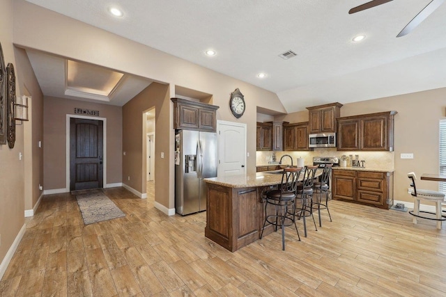 kitchen featuring stainless steel appliances, light wood-style floors, a kitchen bar, a center island with sink, and recessed lighting