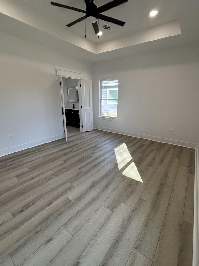 empty room with a raised ceiling, ceiling fan, and light wood-type flooring