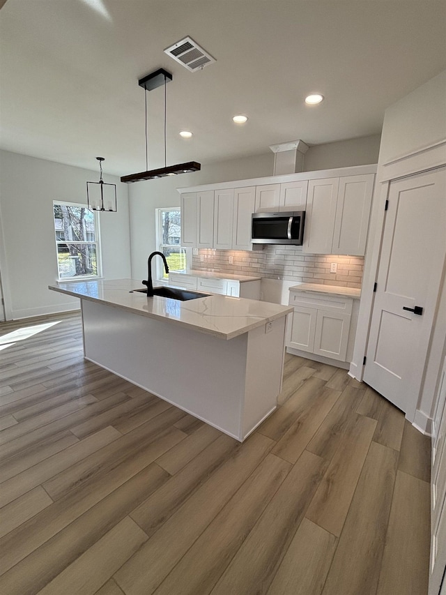 kitchen with sink, tasteful backsplash, hanging light fixtures, an island with sink, and white cabinets