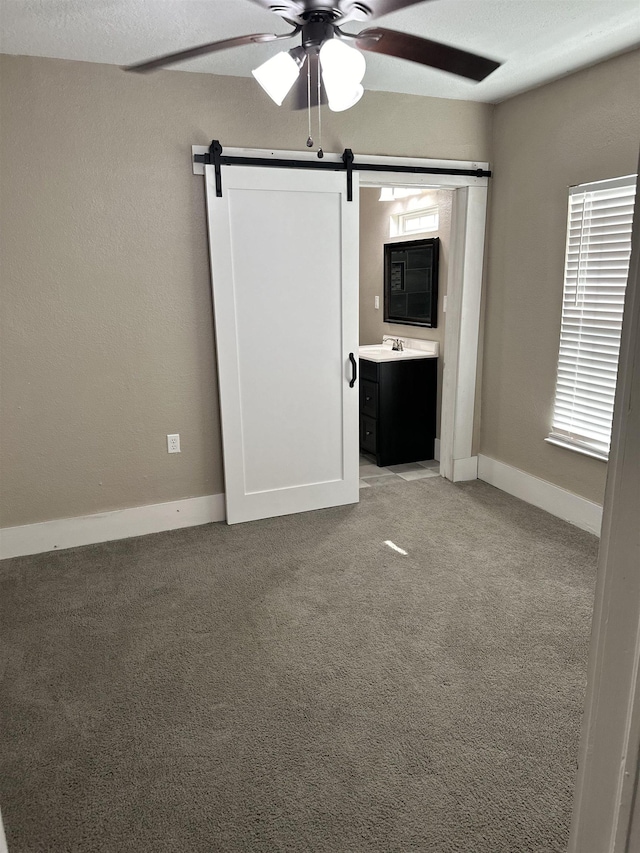 unfurnished bedroom featuring a barn door, carpet floors, ceiling fan, and connected bathroom