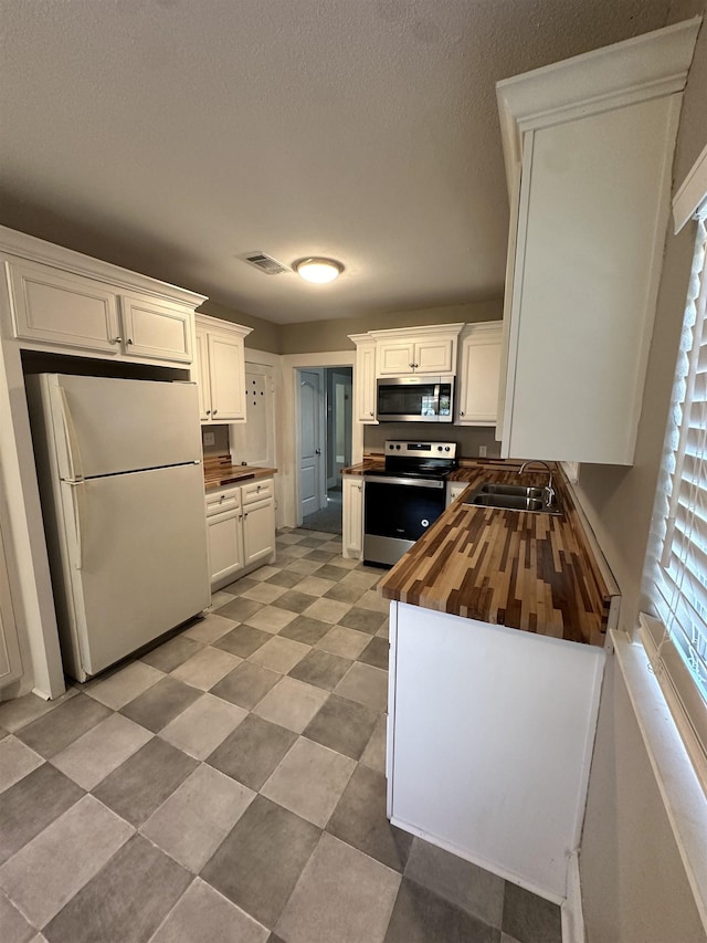 kitchen featuring stainless steel appliances, white cabinetry, butcher block counters, and sink