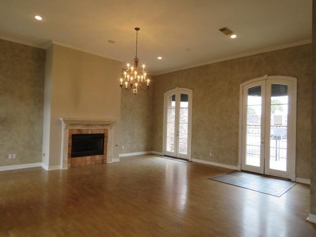 unfurnished living room with a tiled fireplace, crown molding, french doors, and an inviting chandelier