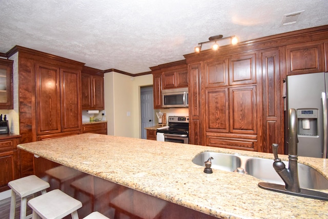 kitchen featuring stainless steel appliances, ornamental molding, light stone countertops, and a breakfast bar area