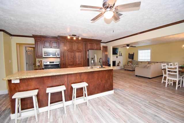 kitchen with a kitchen bar, sink, a textured ceiling, appliances with stainless steel finishes, and light hardwood / wood-style floors