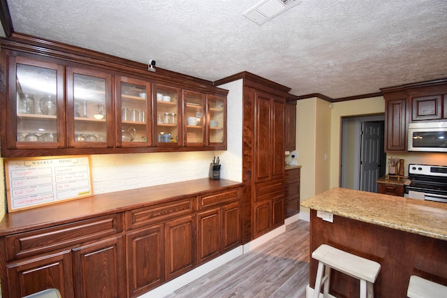 kitchen featuring a textured ceiling, ornamental molding, stainless steel appliances, light stone countertops, and light hardwood / wood-style floors