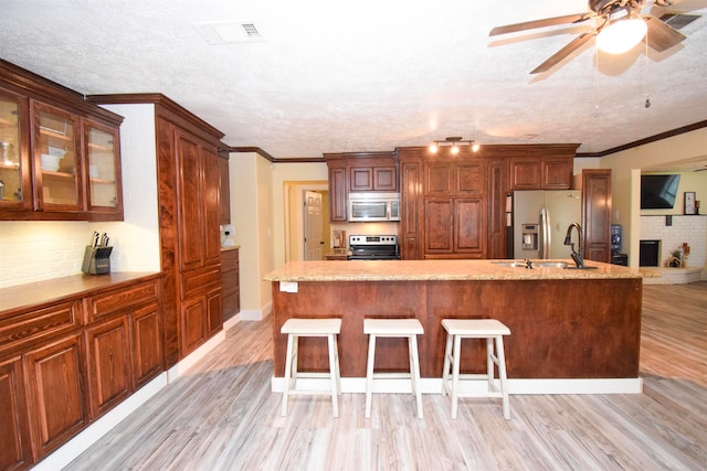 kitchen featuring appliances with stainless steel finishes, a breakfast bar, a textured ceiling, and light hardwood / wood-style flooring