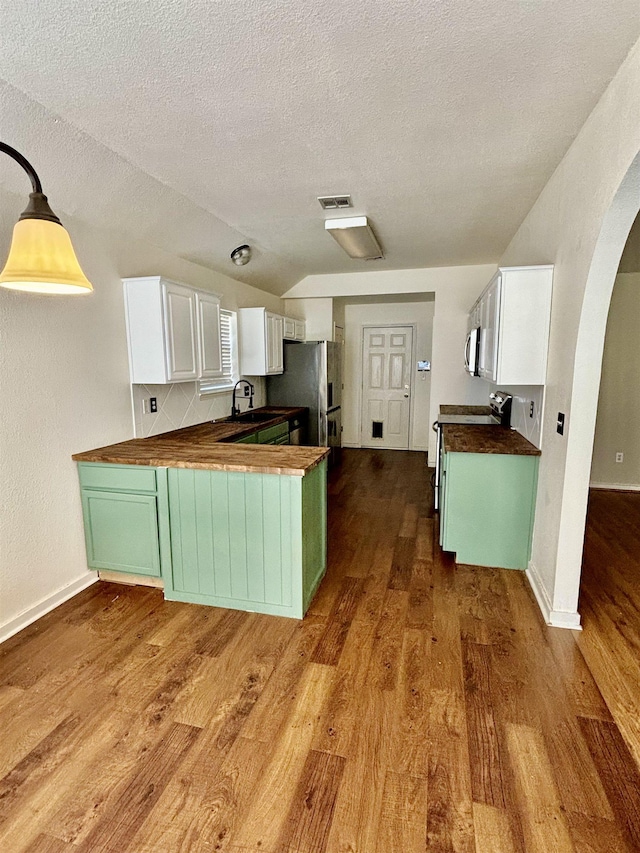 kitchen with kitchen peninsula, stainless steel fridge, a textured ceiling, butcher block countertops, and white cabinetry