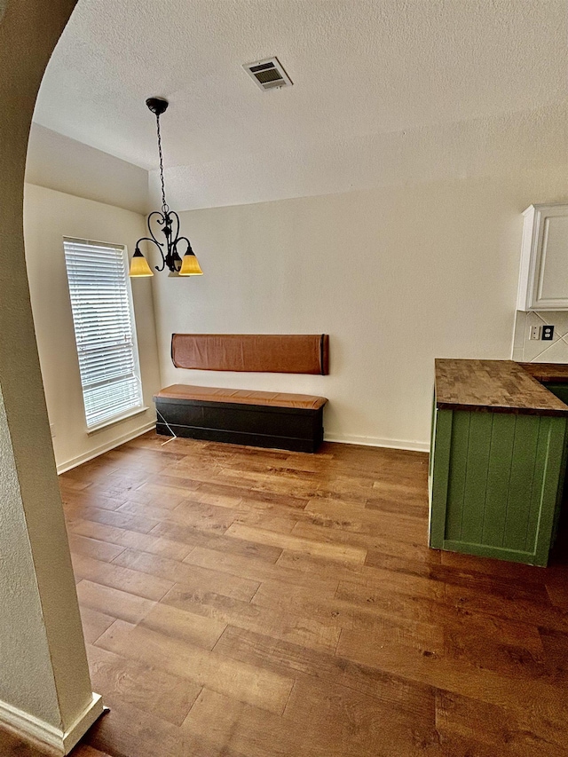 unfurnished dining area featuring a chandelier, a textured ceiling, and hardwood / wood-style flooring