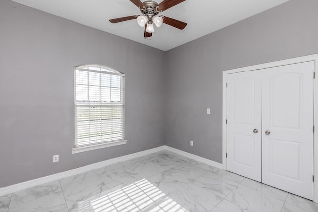 unfurnished bedroom featuring marble finish floor, a ceiling fan, baseboards, and a closet