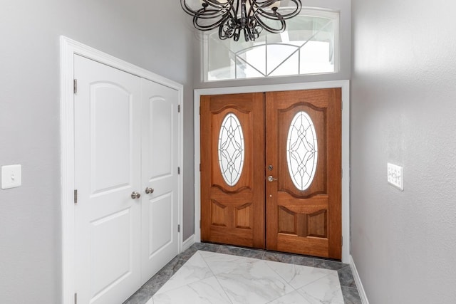 entryway featuring marble finish floor, a notable chandelier, and baseboards