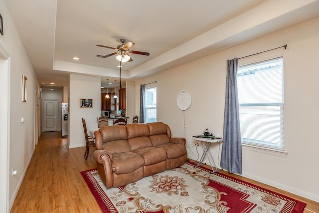 living room with plenty of natural light, light hardwood / wood-style floors, a raised ceiling, and ceiling fan