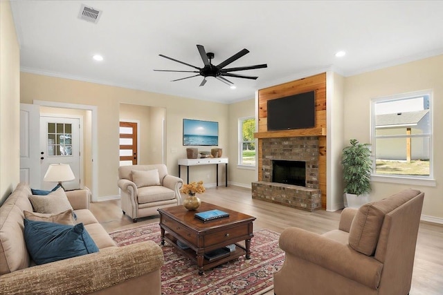 living room with a brick fireplace, crown molding, light hardwood / wood-style flooring, and ceiling fan