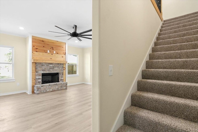 stairway featuring a brick fireplace, hardwood / wood-style flooring, and ceiling fan