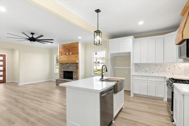 kitchen featuring appliances with stainless steel finishes, white cabinetry, hanging light fixtures, a large fireplace, and a center island with sink