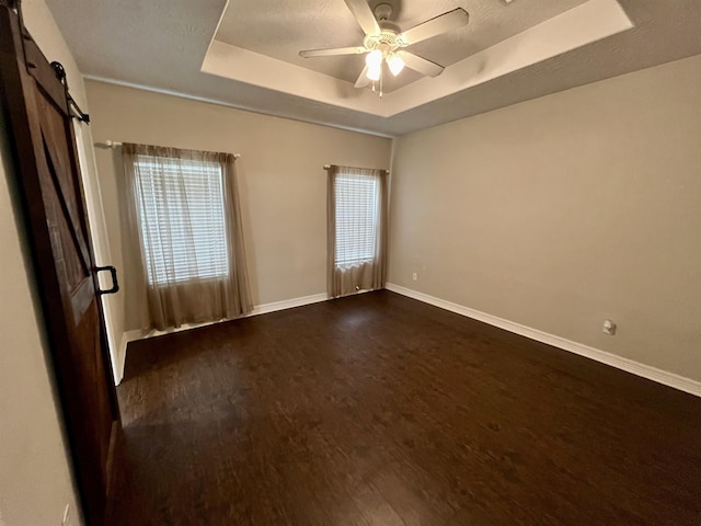 479 Reynolds Ln, Vidor, TX 77662 - unfurnished room featuring a barn door, a ceiling fan, baseboards, dark wood-type flooring, and a tray ceiling