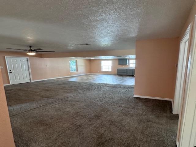 interior space featuring ceiling fan, a textured ceiling, and dark colored carpet