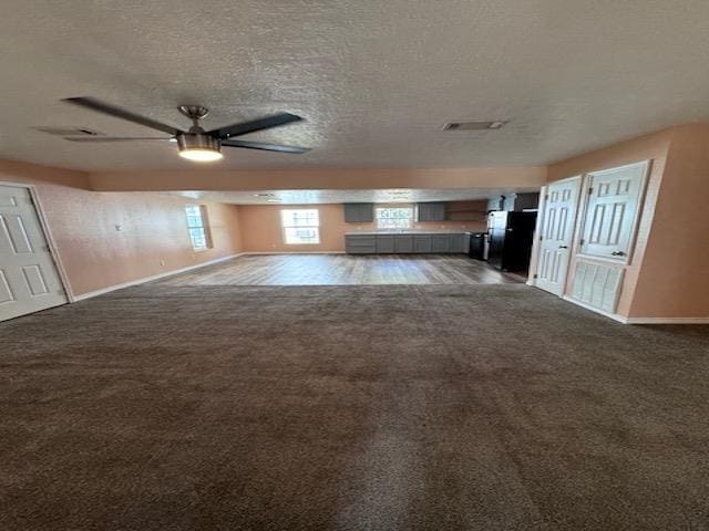 unfurnished living room with ceiling fan, dark carpet, and a textured ceiling