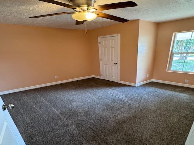 empty room with dark colored carpet, ceiling fan, and a textured ceiling