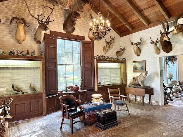 sitting room featuring beam ceiling, high vaulted ceiling, brick wall, and a notable chandelier