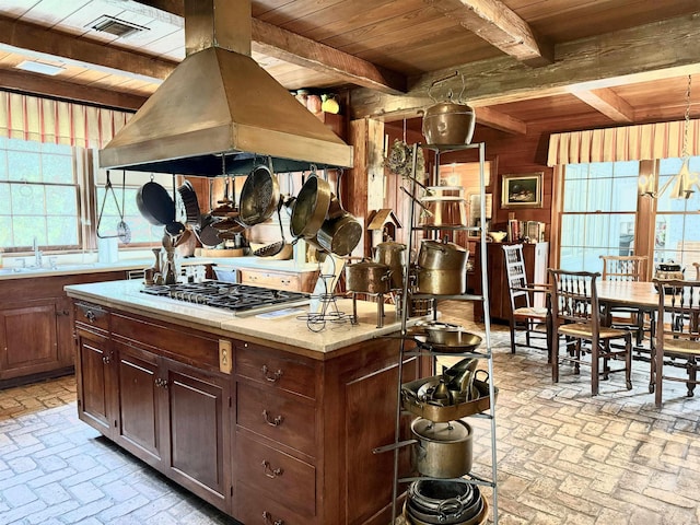 kitchen with a center island, beamed ceiling, stainless steel gas stovetop, wood ceiling, and custom range hood