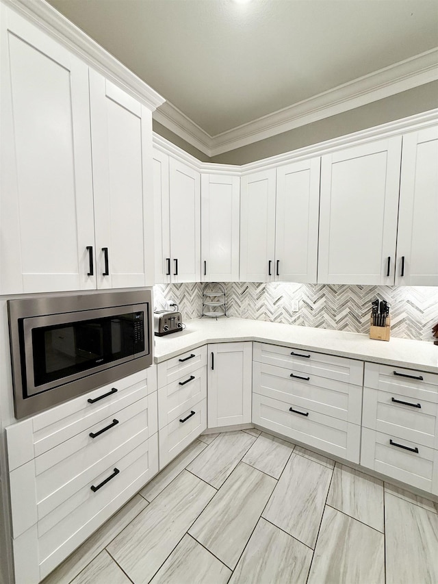 kitchen featuring stainless steel microwave, crown molding, decorative backsplash, and white cabinets