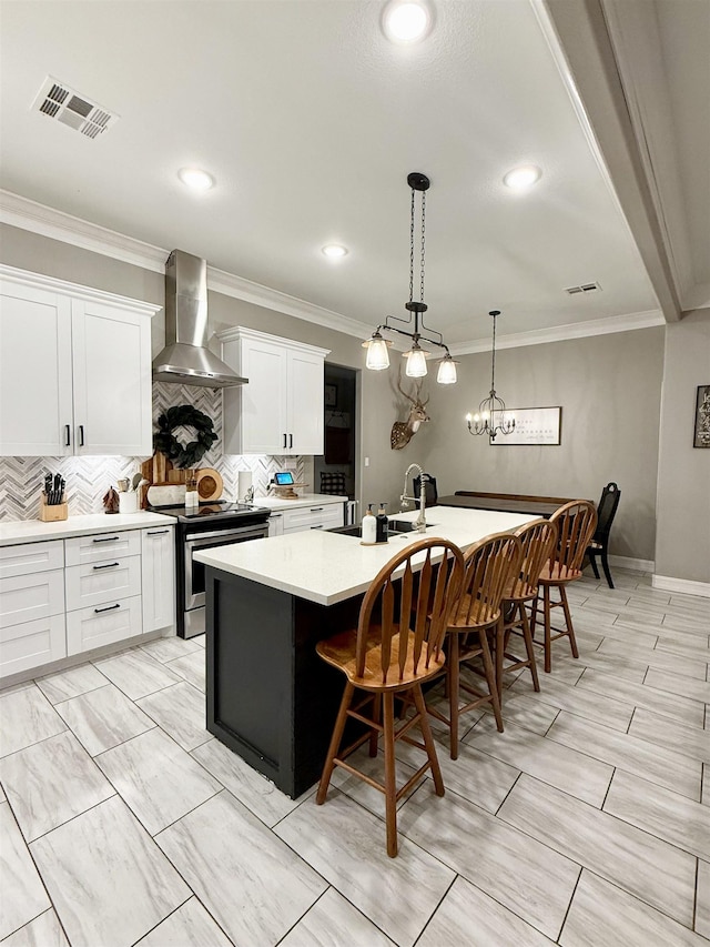 kitchen with a kitchen bar, white cabinetry, stainless steel electric range, an island with sink, and wall chimney range hood