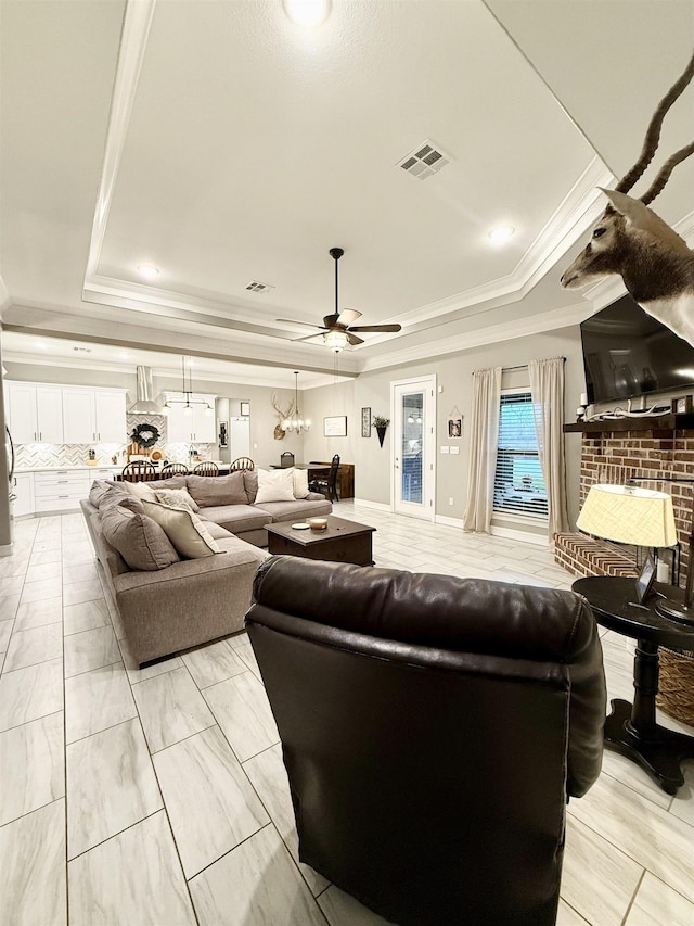 living room with crown molding, ceiling fan, a tray ceiling, and a fireplace