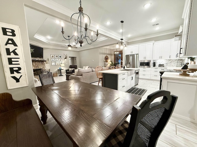 dining room featuring sink, a tray ceiling, a fireplace, ornamental molding, and a chandelier