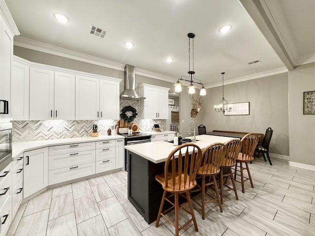 kitchen featuring a breakfast bar area, white cabinetry, hanging light fixtures, a kitchen island with sink, and wall chimney range hood