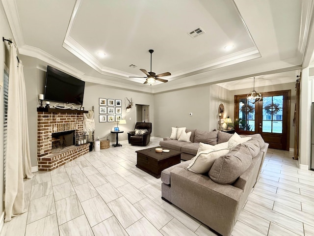 living room with crown molding, a brick fireplace, ceiling fan, and a tray ceiling