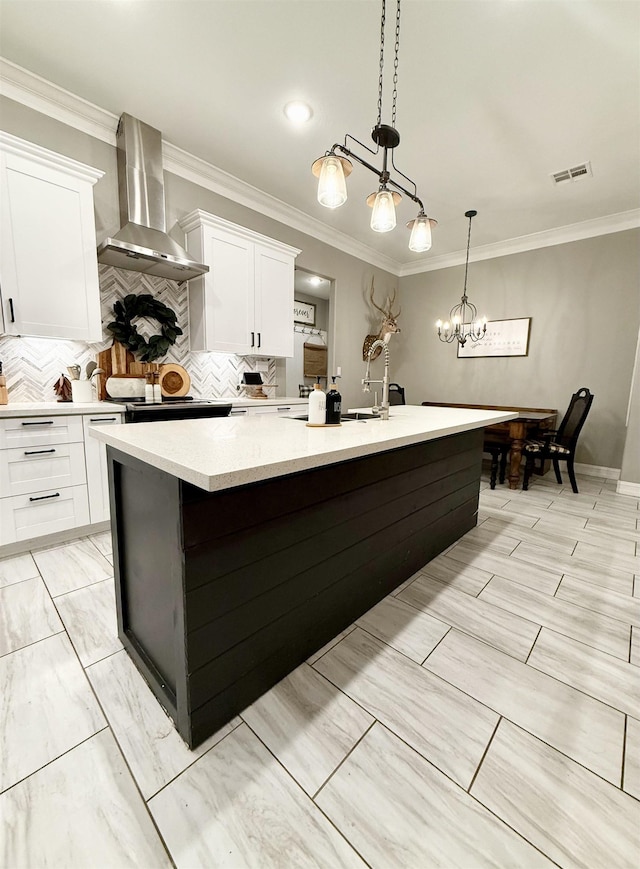 kitchen with white cabinets, decorative light fixtures, a center island with sink, and wall chimney range hood