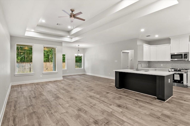 kitchen featuring a kitchen island with sink, a raised ceiling, sink, white cabinetry, and stainless steel appliances