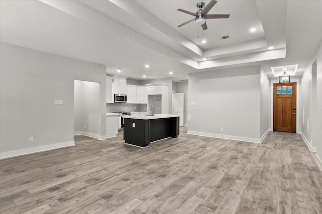 kitchen with a kitchen island with sink, white cabinets, sink, a tray ceiling, and stainless steel appliances