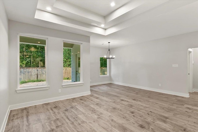 spare room with a notable chandelier, light hardwood / wood-style floors, and a raised ceiling