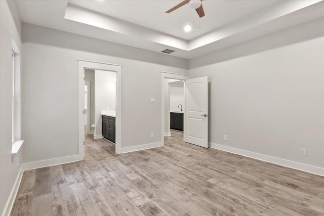 unfurnished bedroom with light hardwood / wood-style flooring, a raised ceiling, ceiling fan, and ensuite bathroom