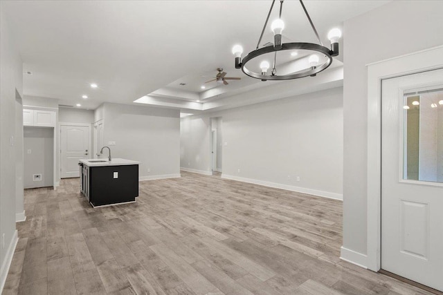 interior space with ceiling fan with notable chandelier, light wood-type flooring, sink, and a tray ceiling