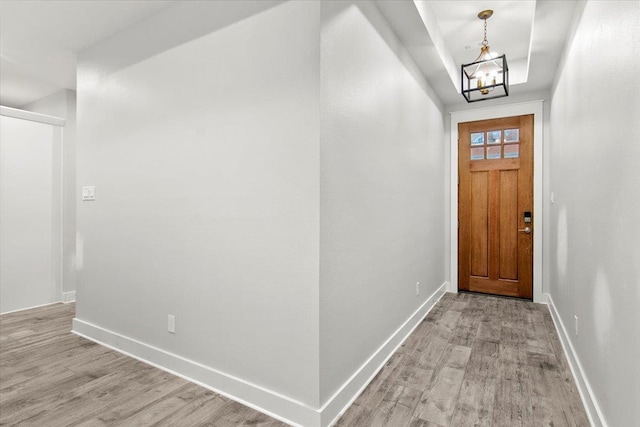 foyer featuring a raised ceiling, light wood-type flooring, and a chandelier