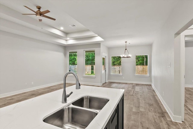 kitchen with light stone countertops, sink, a raised ceiling, pendant lighting, and light hardwood / wood-style floors