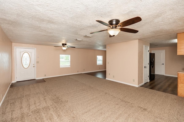 unfurnished living room with baseboards, a ceiling fan, dark carpet, and a textured ceiling