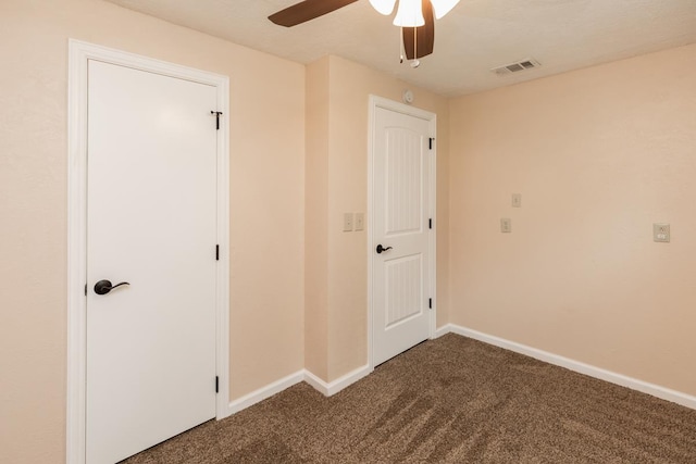 unfurnished bedroom featuring visible vents, baseboards, dark carpet, and ceiling fan