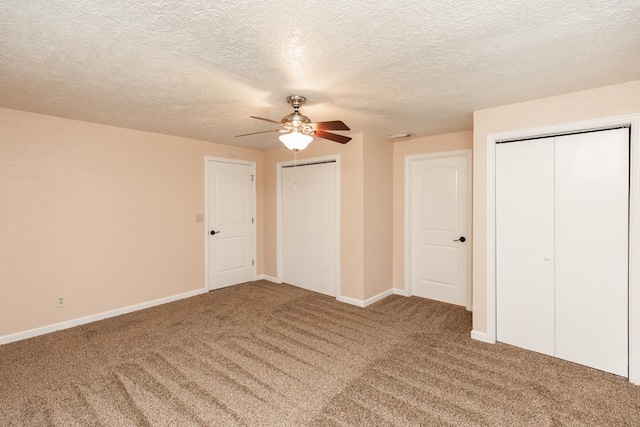 unfurnished bedroom featuring carpet floors, a textured ceiling, baseboards, and two closets