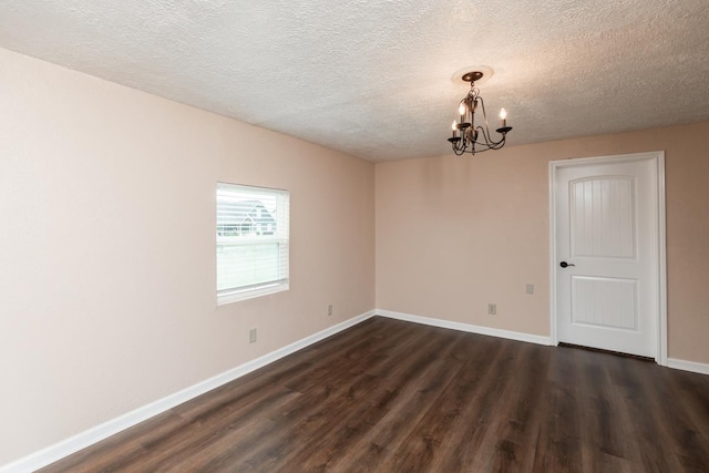 spare room with an inviting chandelier, baseboards, dark wood-style floors, and a textured ceiling