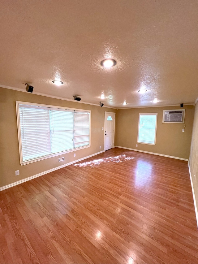 unfurnished room featuring light wood-type flooring, an AC wall unit, a textured ceiling, and ornamental molding