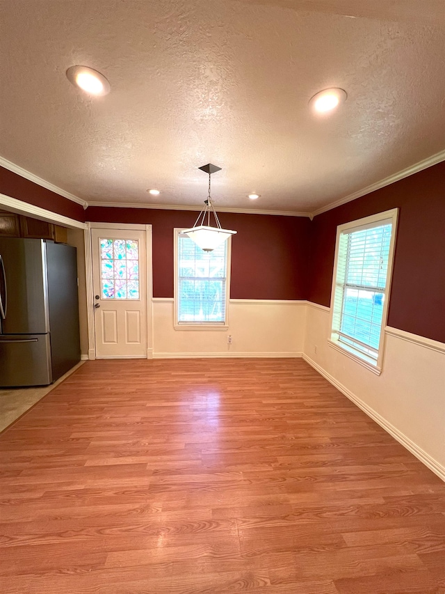 unfurnished dining area with a textured ceiling, light hardwood / wood-style floors, and ornamental molding