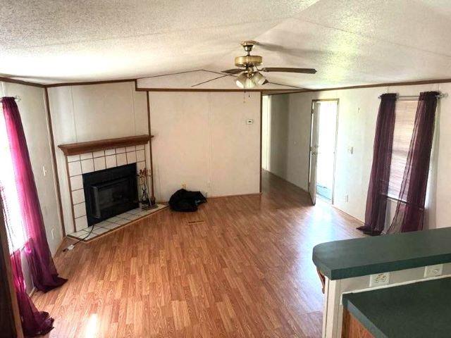 unfurnished living room with a textured ceiling, vaulted ceiling, ceiling fan, a tile fireplace, and hardwood / wood-style floors