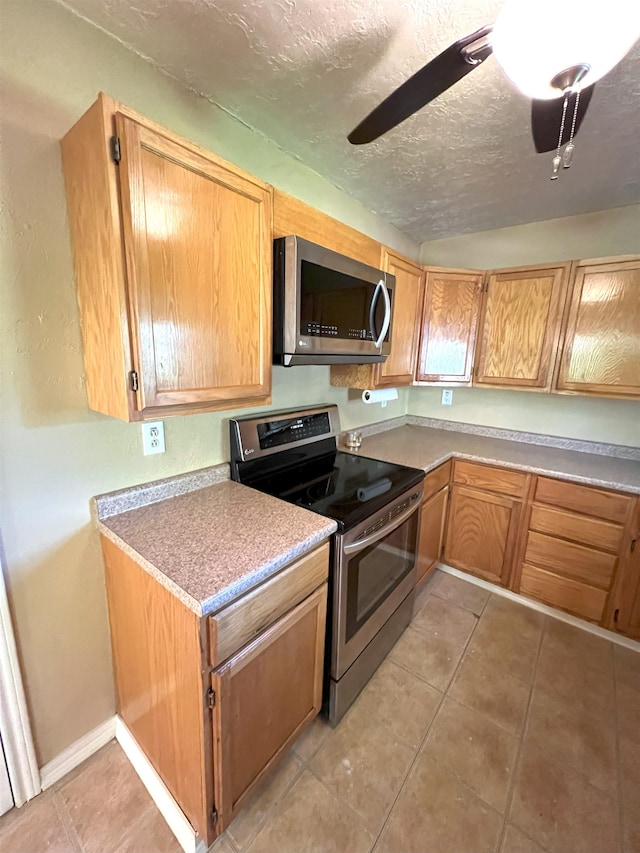 kitchen featuring ceiling fan, light tile patterned floors, stainless steel appliances, and a textured ceiling