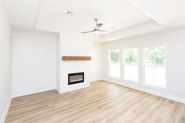 unfurnished living room with a raised ceiling, ceiling fan, a large fireplace, and light wood-type flooring